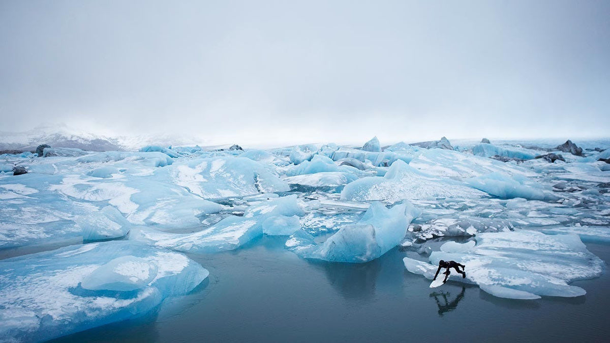 Surfer jumping into the ocean surrounded by icebergs