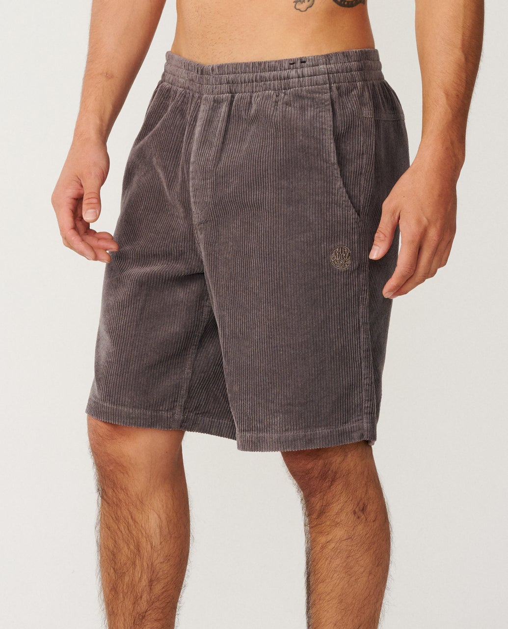 A person wearing gray corduroy shorts with an elastic waistband, standing against a plain background.