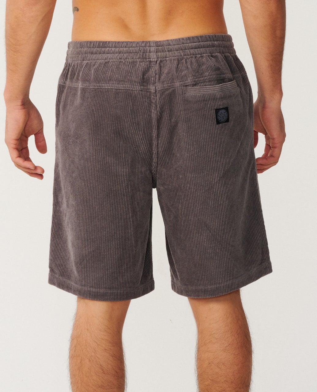 A person is shown from the back, wearing gray corduroy shorts with an elastic waistband and a small pocket.