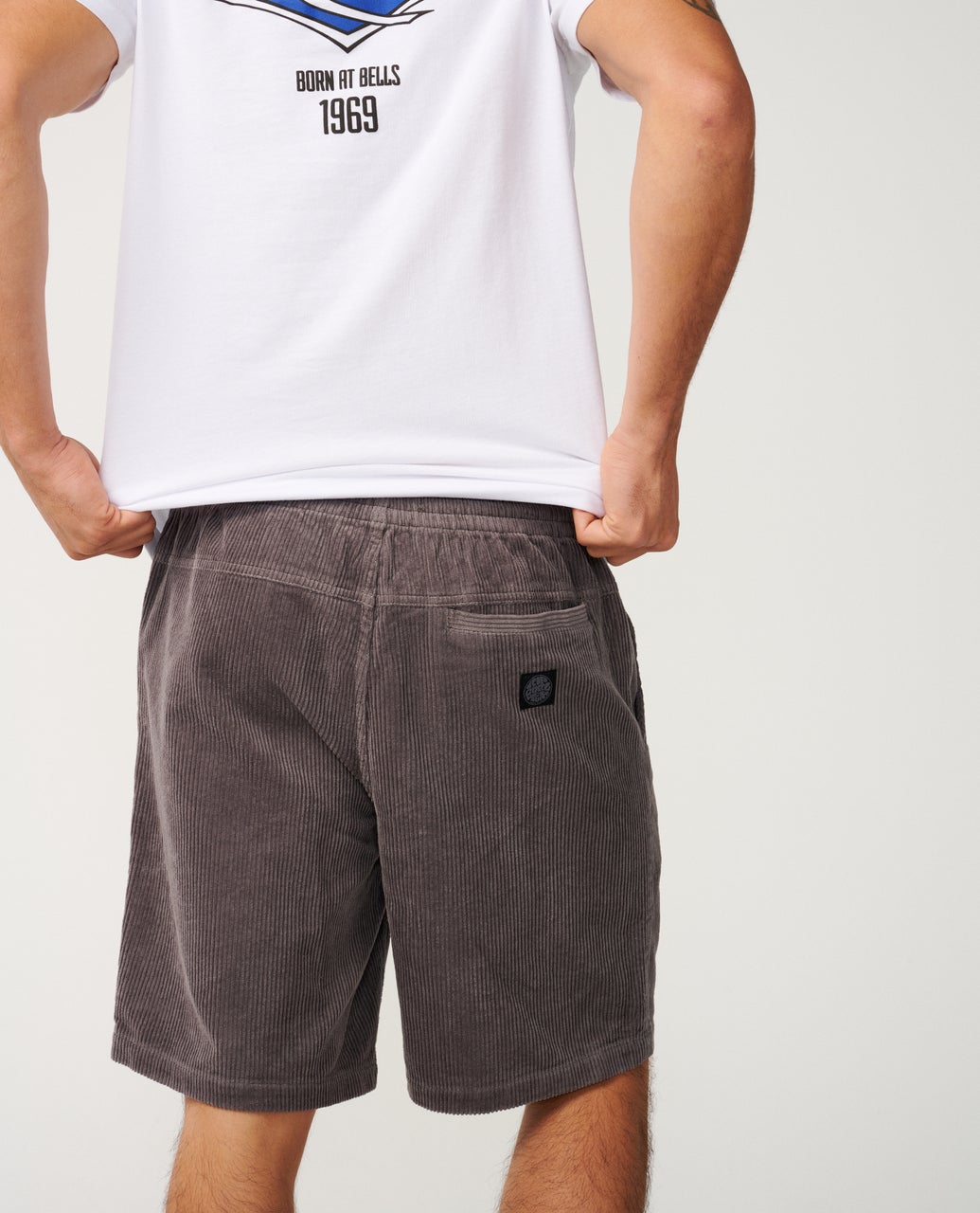 A person is seen from behind, wearing a white t-shirt and gray corduroy shorts with a back pocket.