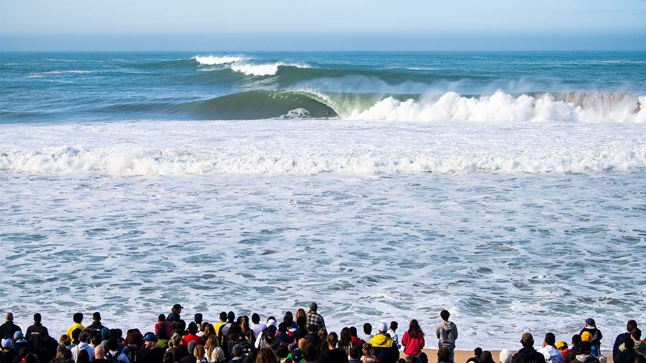 Surfers and spectators at a beach with waves crashing in the background