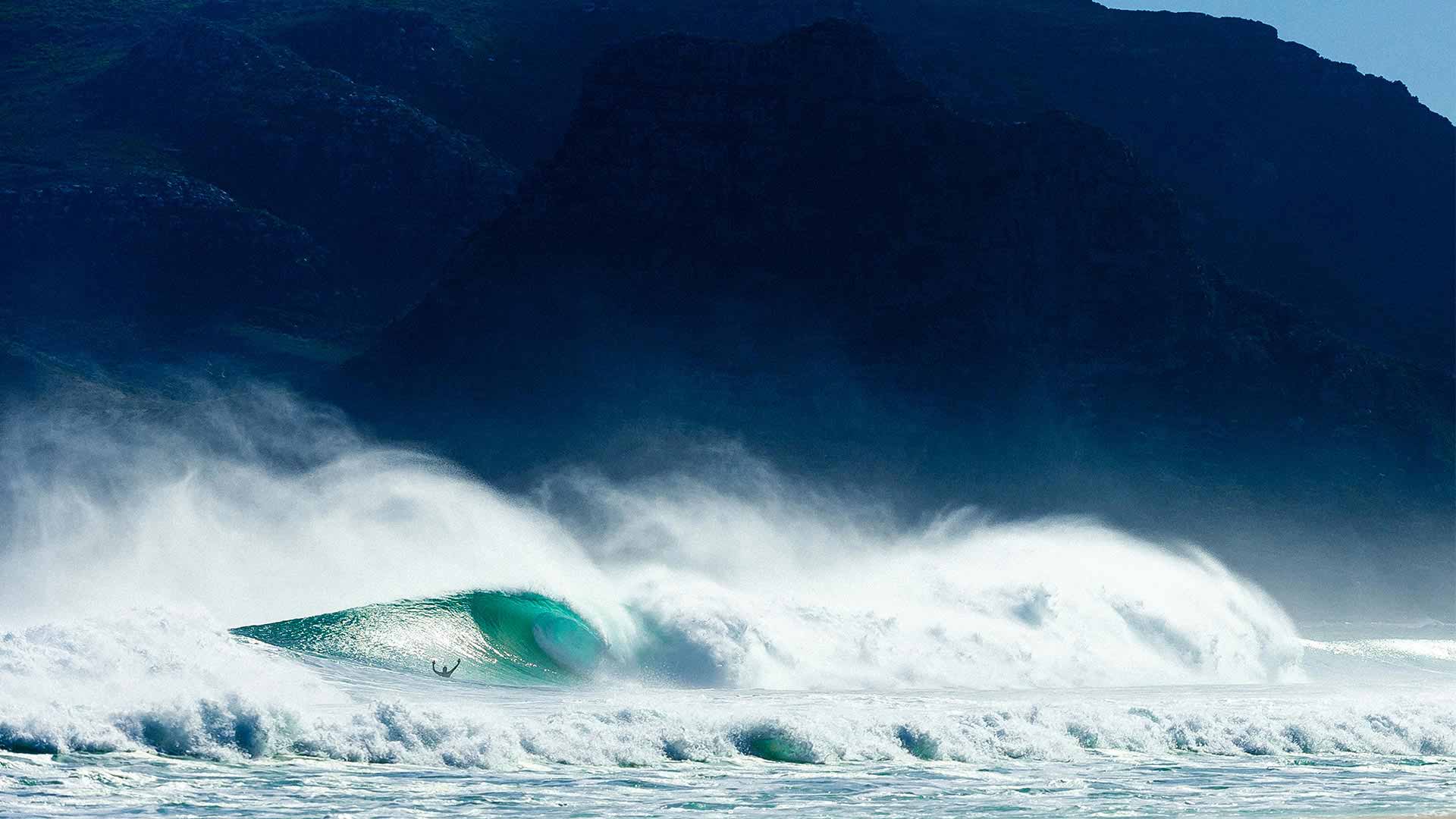 Surfer riding a large wave with a mountainous background