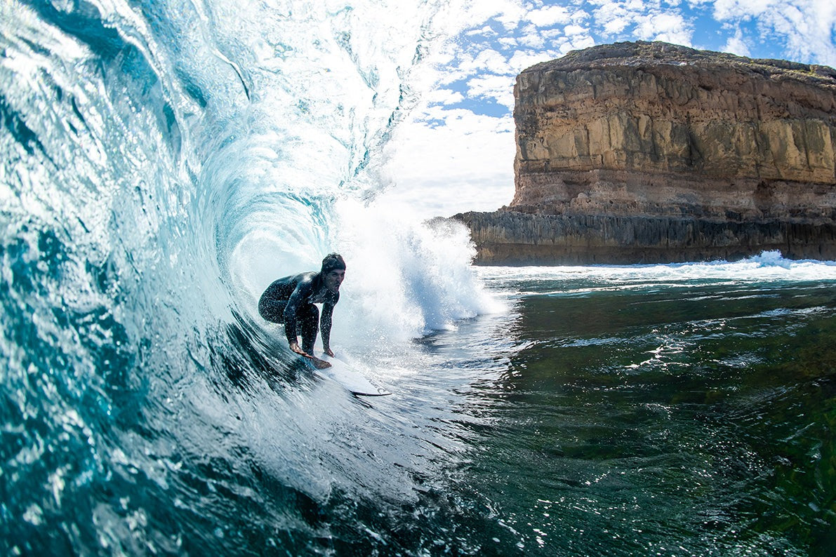 Person surfing inside a wave with a rocky outcrop in the background