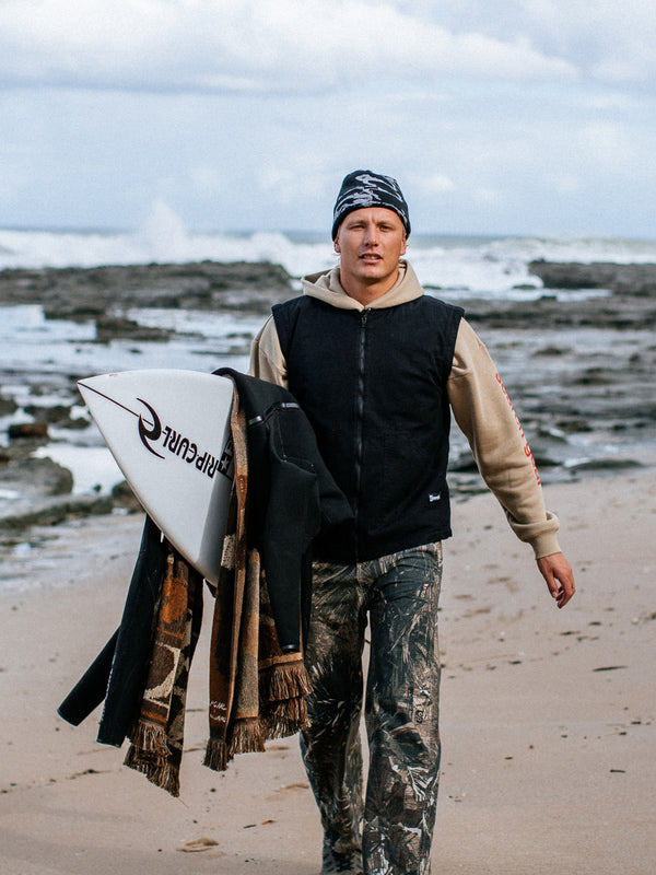 Person holding a surfboard on a beach with waves and rocks in the background