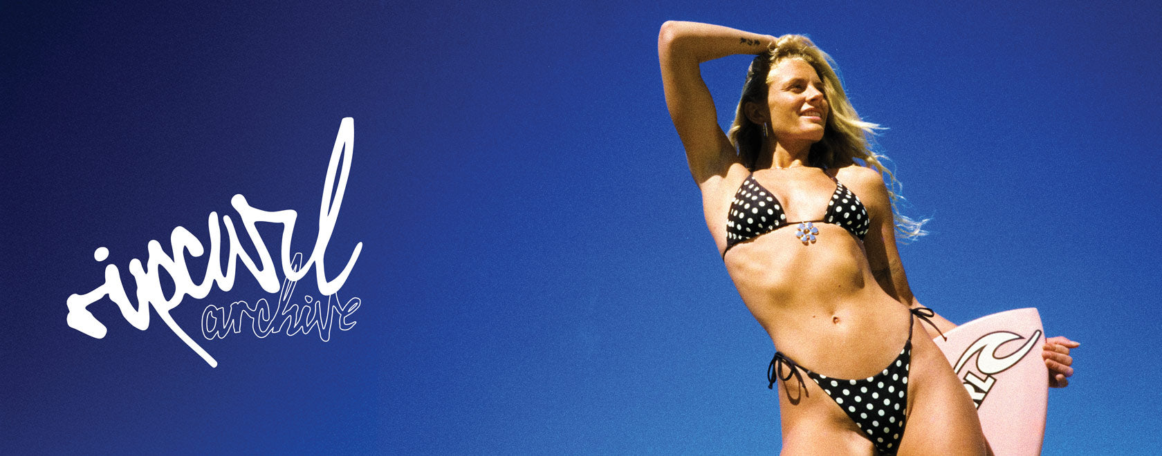 Woman in a polka dot bikini with a surfboard against a blue sky, featuring Rip Curl logo.