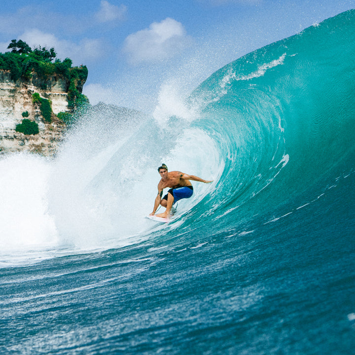 Surfer riding a large wave with a cliff and greenery in the background