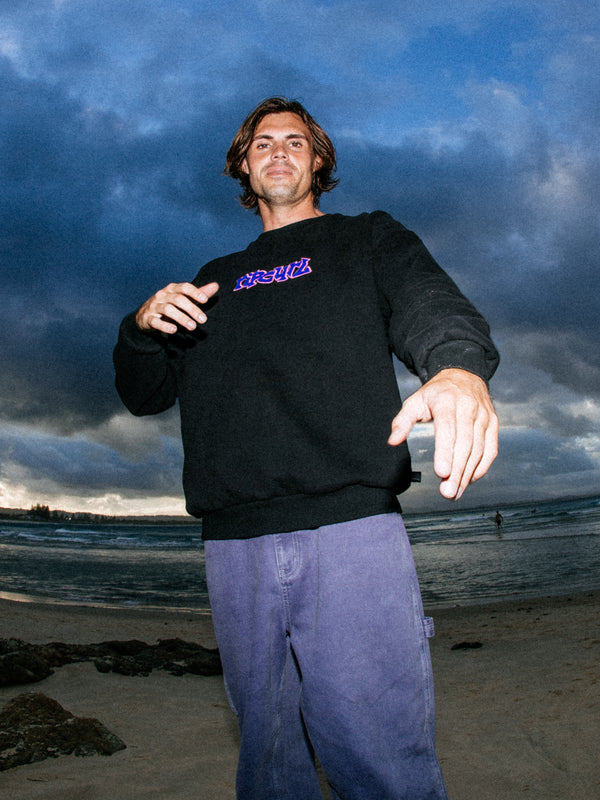 Man wearing a black sweatshirt with a logo on a beach with dark clouds in the sky