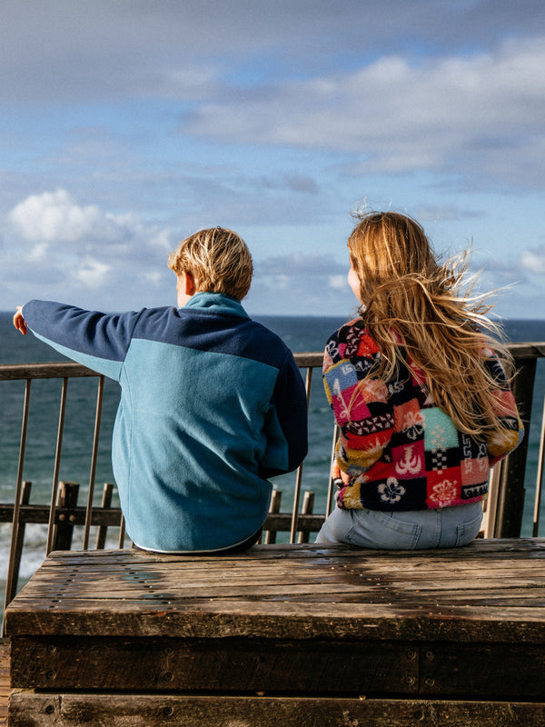 Two people sitting at a wooden table overlooking the ocean with a cloudy sky.