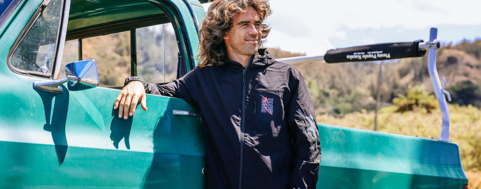 Man leaning against a vintage green truck with a scenic background