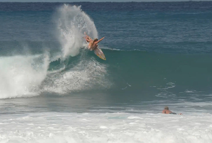 Surfer performing a trick on a wave with another surfer in the water.