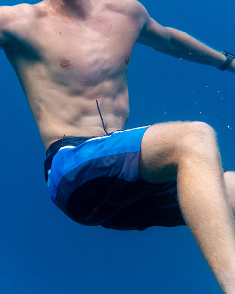 Person wearing blue boardshorts shorts underwater with a clear blue background