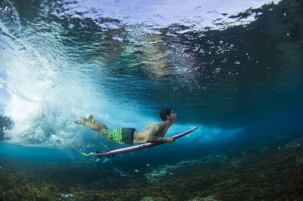 Person swimming with a surfboard underwater in clear blue water