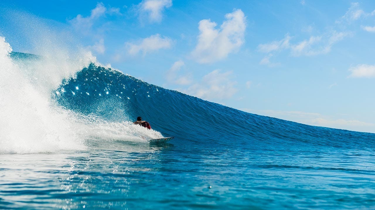 Person surfing a large wave in the ocean with a clear blue sky.