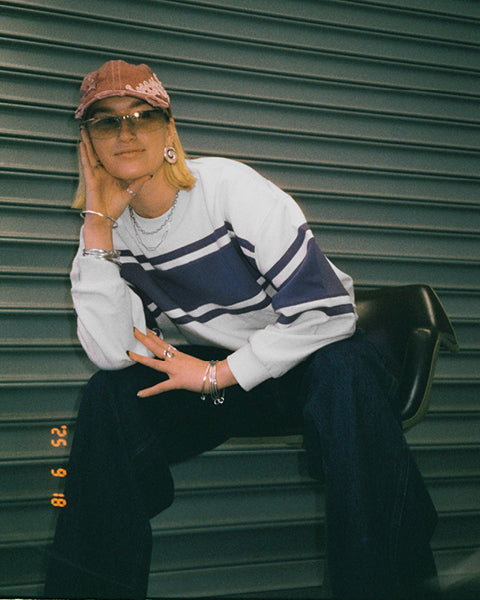 Person wearing a white and blue striped sweater with a red cap sitting against a green shutter.