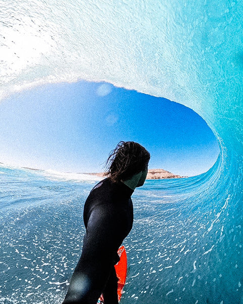 Person surfing inside a wave with clear blue water and sky.