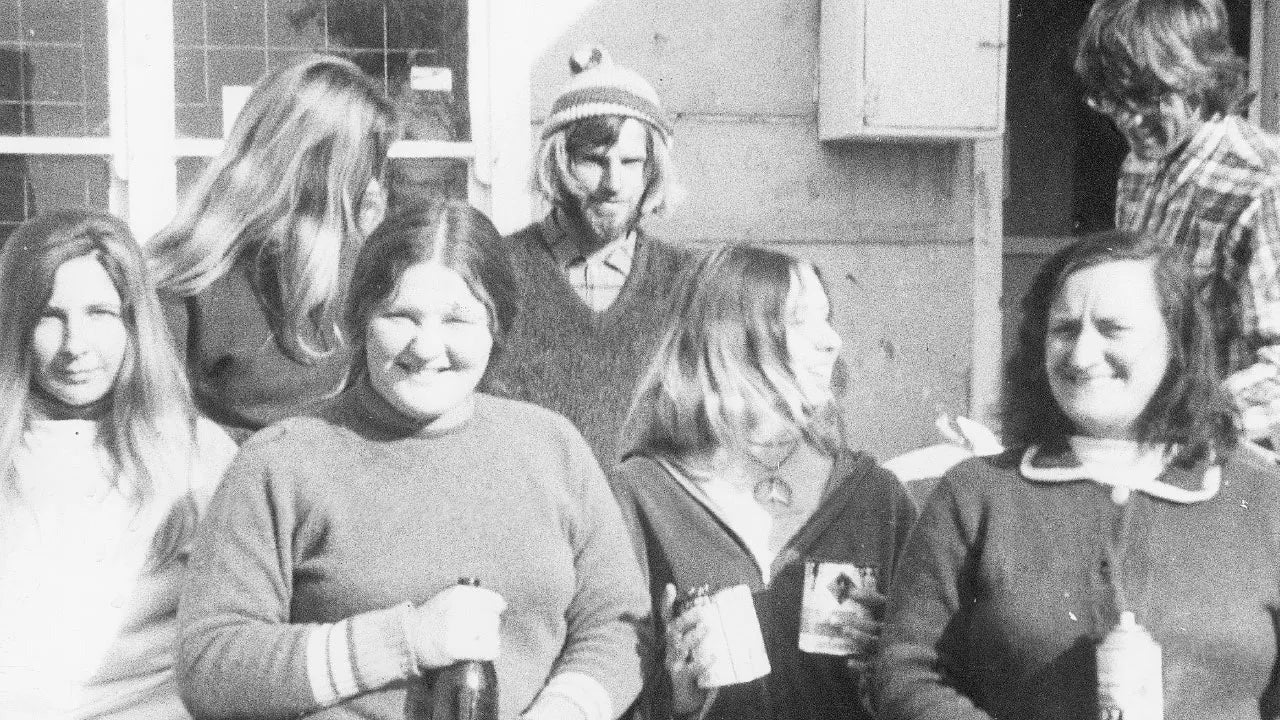 Black and white photo of a group of people standing outdoors, wearing sweaters and jackets.
