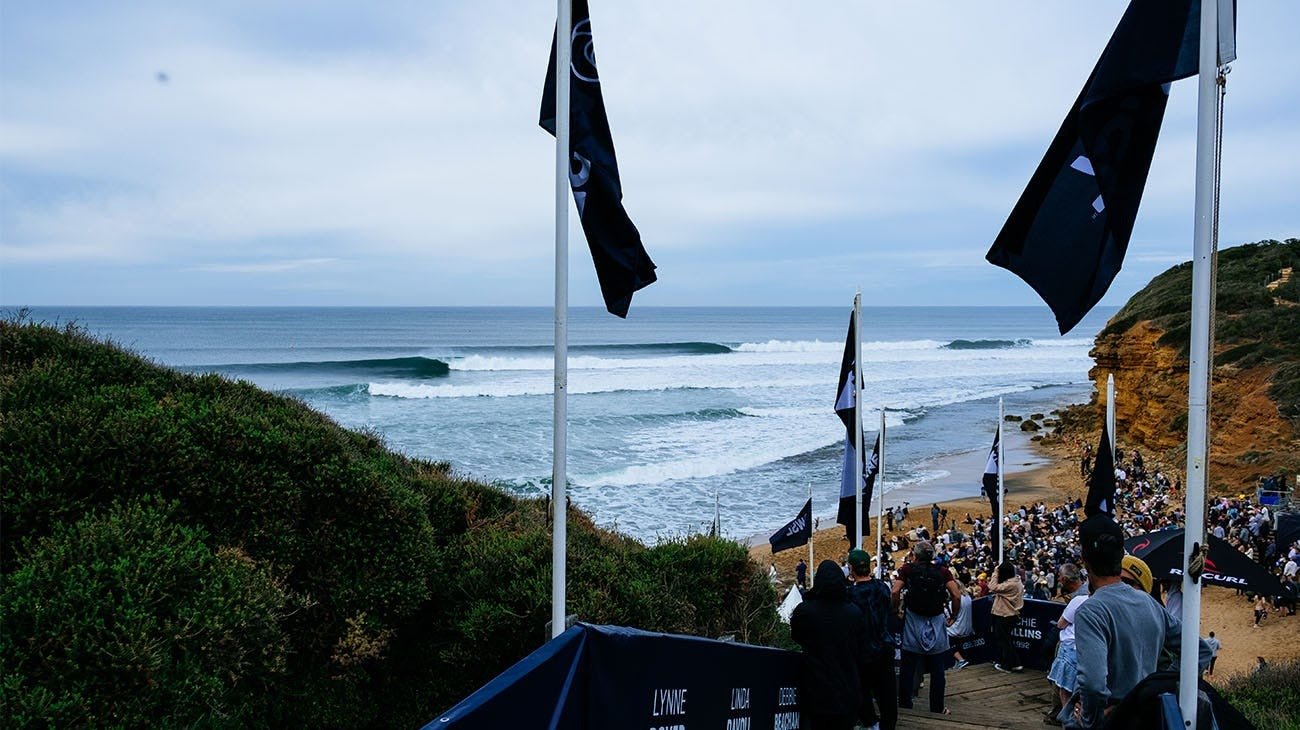 Surfing event with spectators and flags overlooking the ocean.