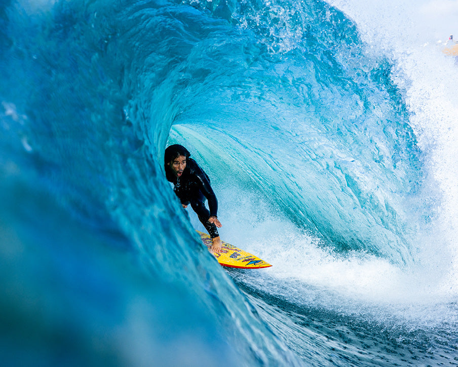Person surfing inside a large blue wave on a yellow surfboard.