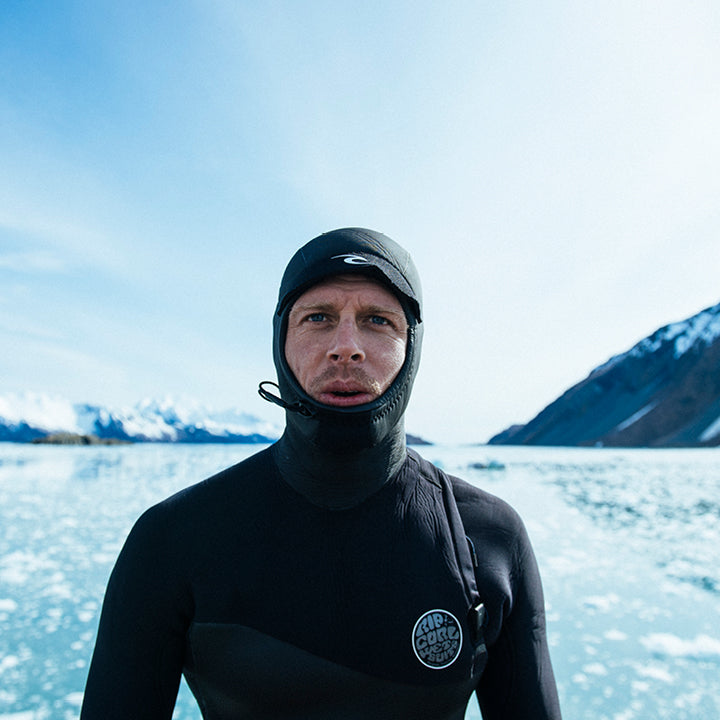Person wearing a black wetsuit with a hood in a snowy landscape