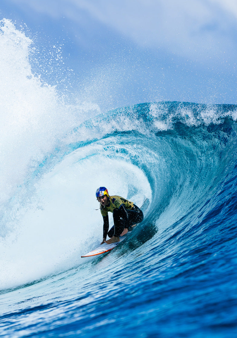 Surfer riding a large wave in the ocean with clear blue sky.