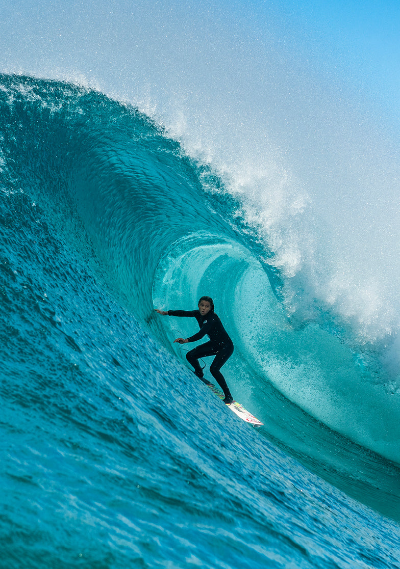 Surfer in a black wetsuit riding a large blue wave.