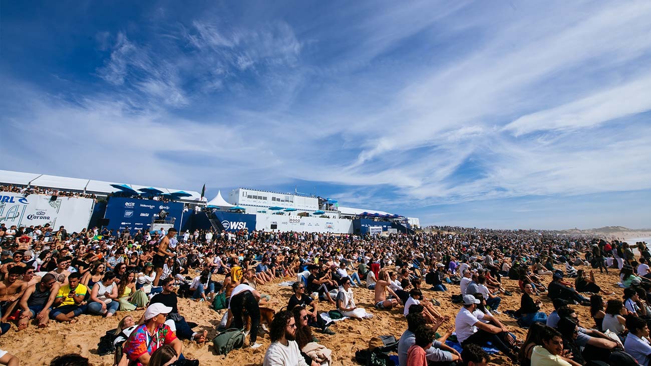 Large crowd at a desert event with tents and vehicles under a blue sky.
