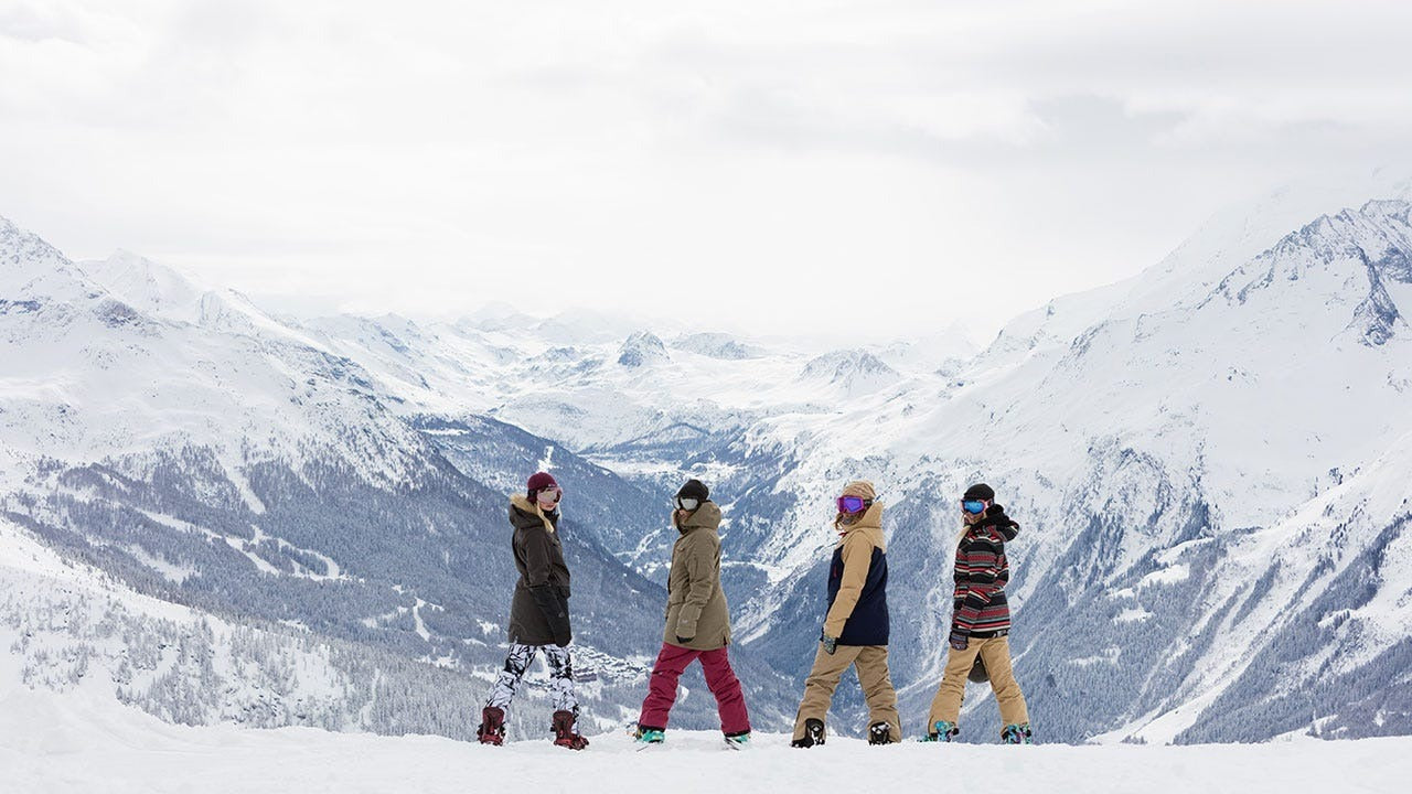 Four people standing on a snowy slope with mountains in the background