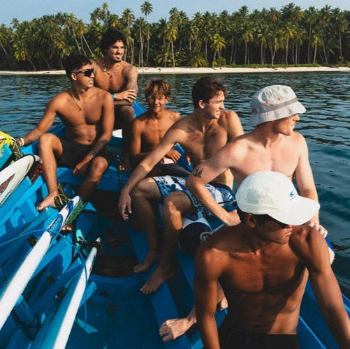 Group of young men on a blue boat in a tropical setting with palm trees and clear water.
