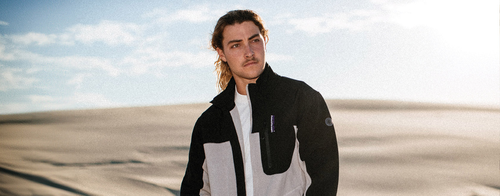 Man wearing a black and white jacket standing in a desert landscape with a clear sky.