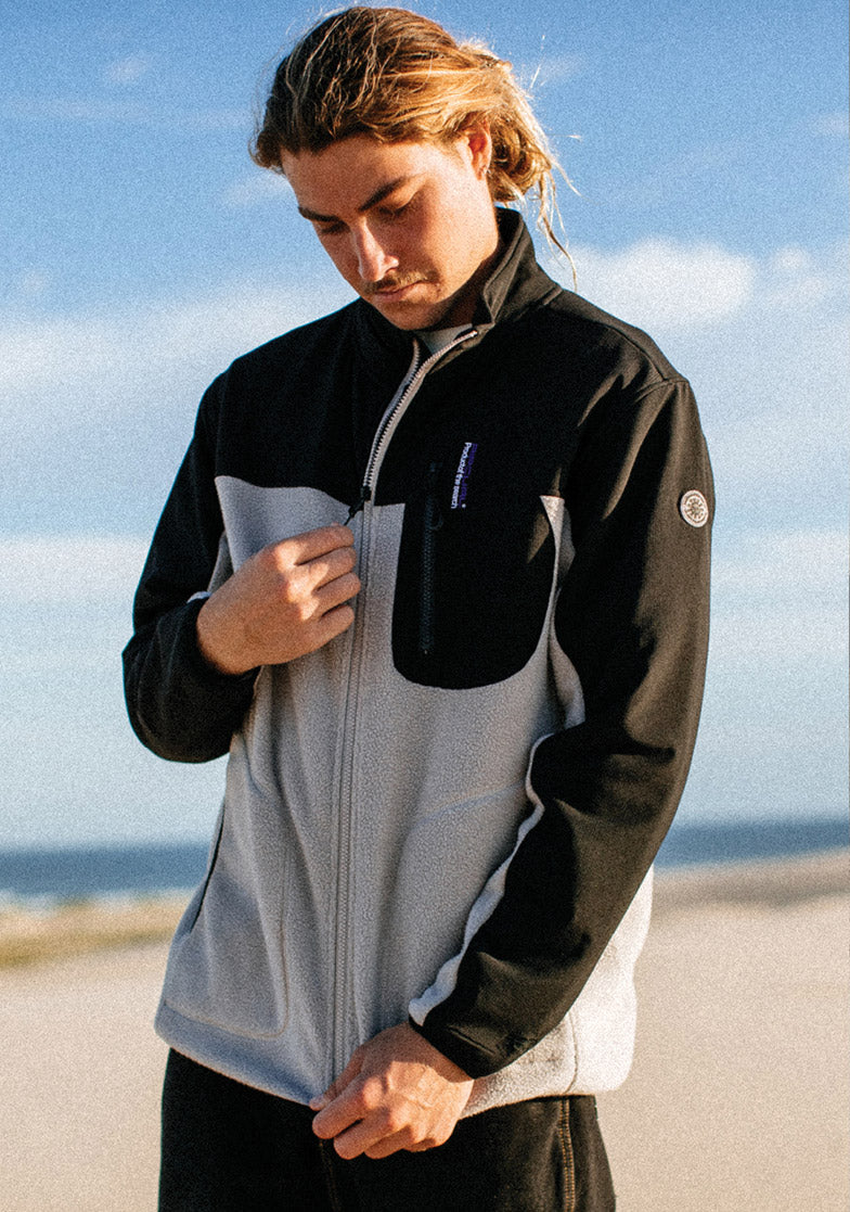 Person wearing a black and gray jacket with a blue sky and ocean background