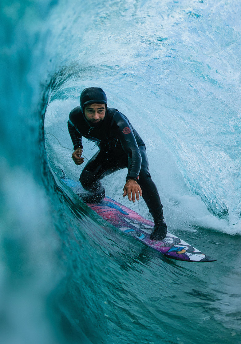 Surfer in a black wetsuit riding a wave on a colorful surfboard.
