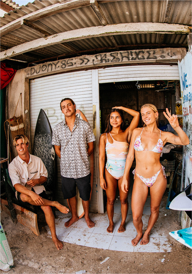 Group of people posing in front of a surf shop with surfboards.