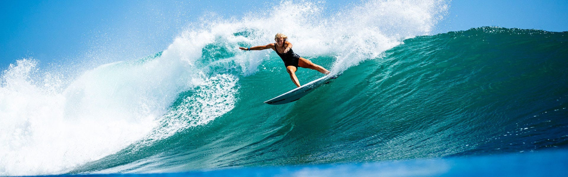 Person surfing on a large wave with clear blue sky