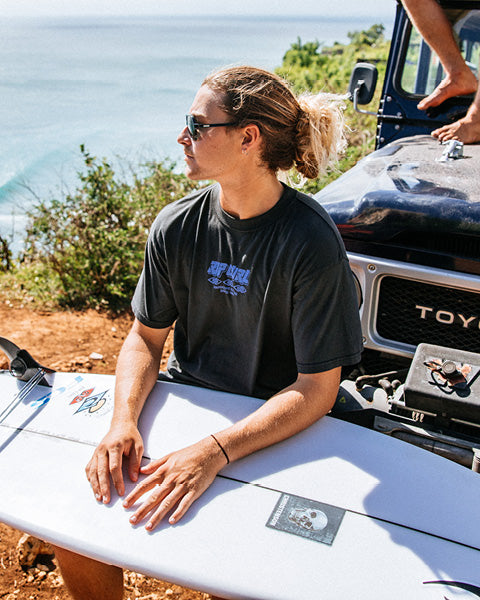 Person sitting on a surfboard with a Toyota vehicle in the background