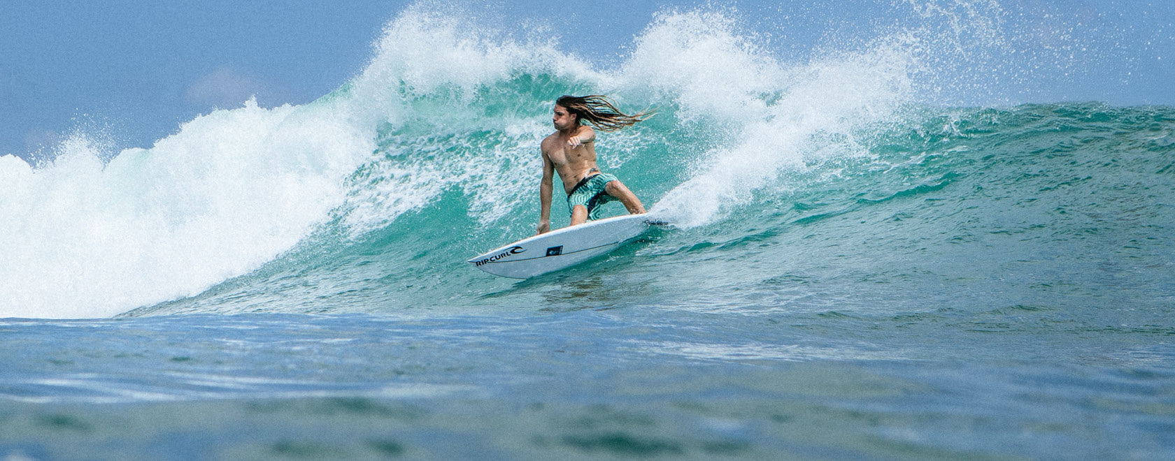 Person surfing on a wave in the ocean with clear blue sky.