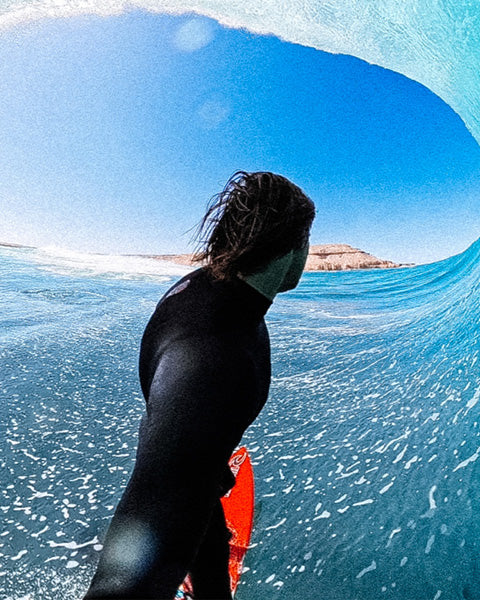 Person in a wetsuit inside a curling wave with clear blue sky.
