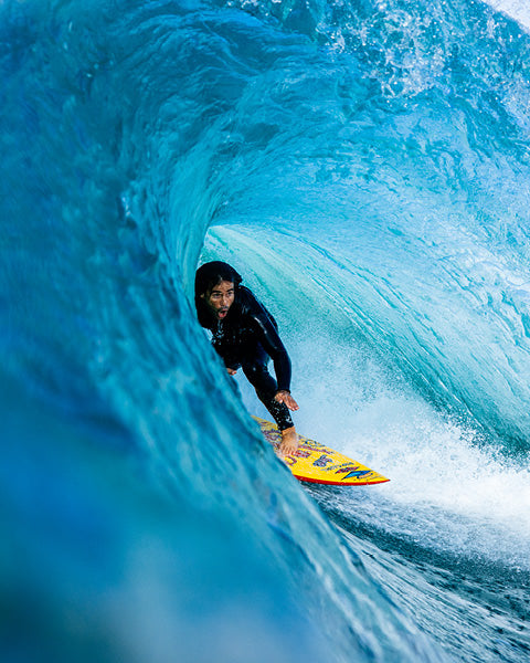 Person surfing on a yellow surfboard inside a blue wave.