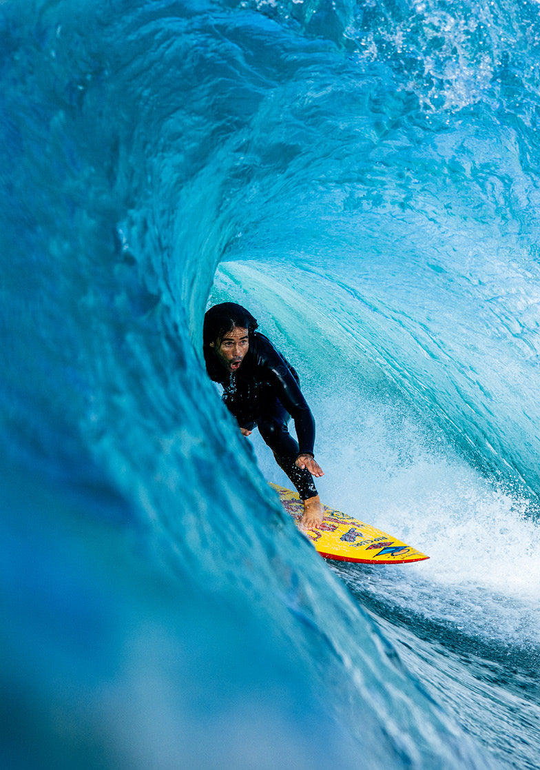 Surfer riding a large wave in a black wetsuit with a yellow surfboard.