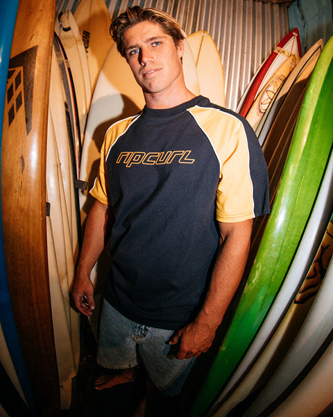 Man wearing a Rip Curl shirt standing among surfboards