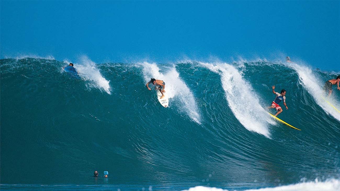Surfers riding a large wave in the ocean with clear blue sky.