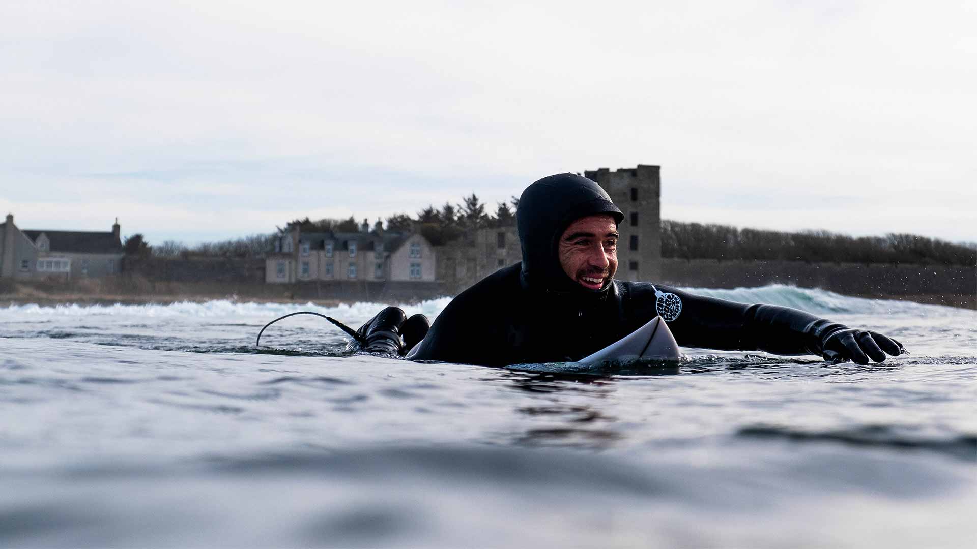 Mason Ho paddling out in a Rip Curl winter wetsuit, hood and booties.