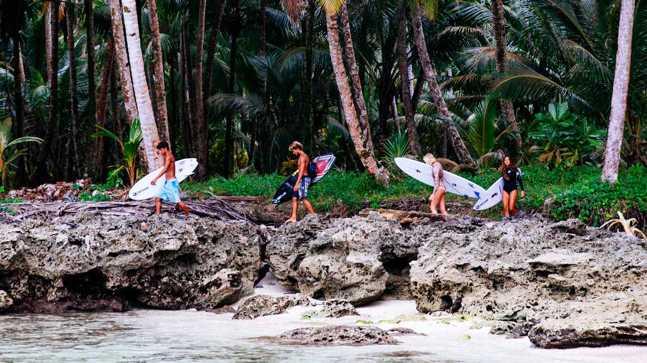 Crew carrying their boards walking across rocks