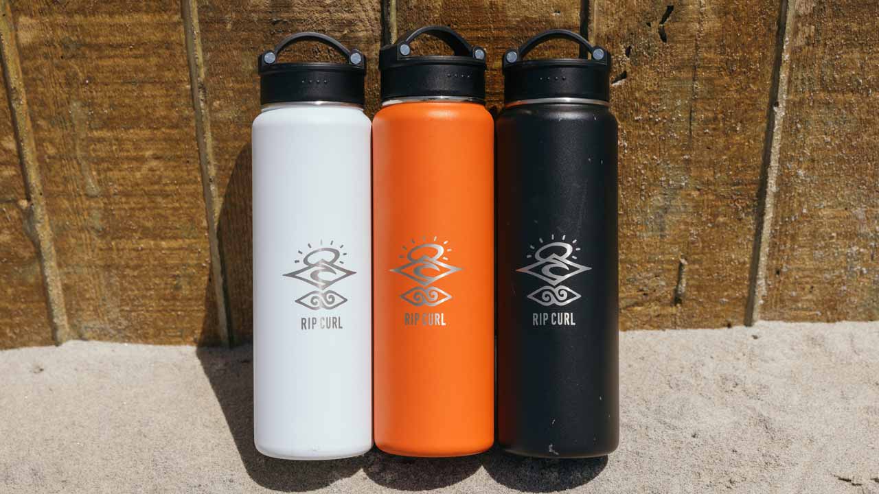 A white, orange and black "The Search Drink Bottle" standing up against a fence.