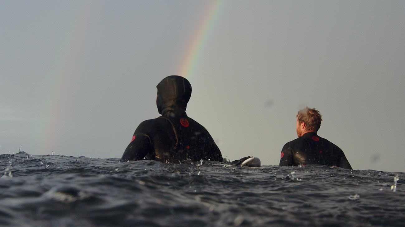 Rip Curl crew sitting on their boards in the ocean with a rainbow in the background