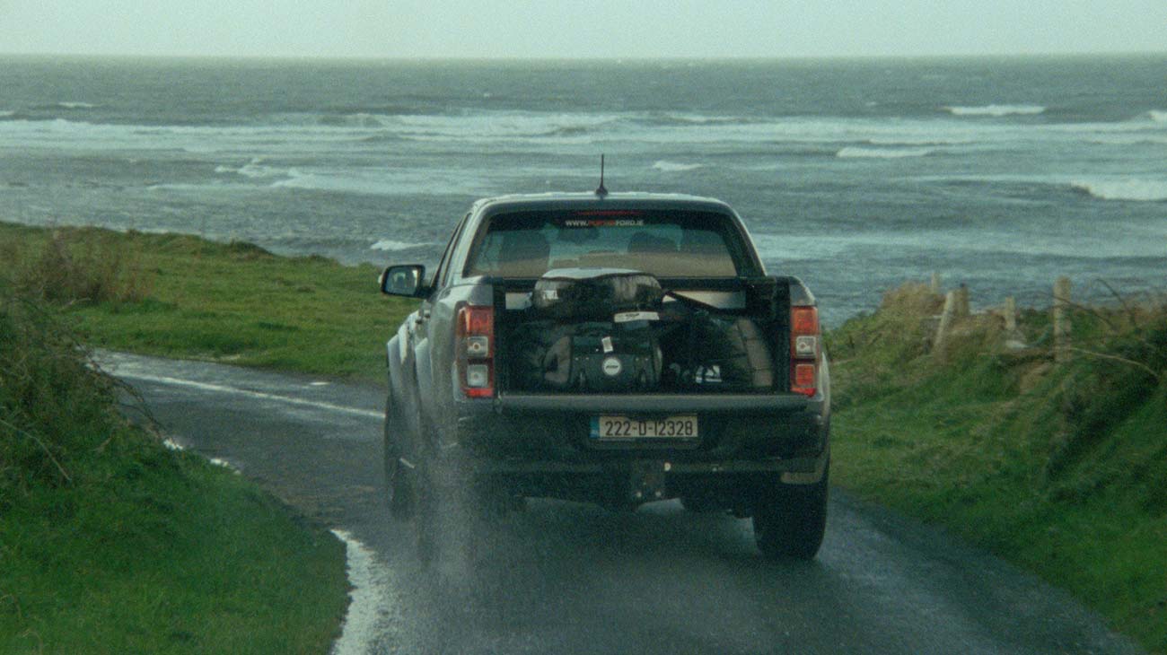 A ute tray full of surfboard bags driving along the cliffs of Ireland