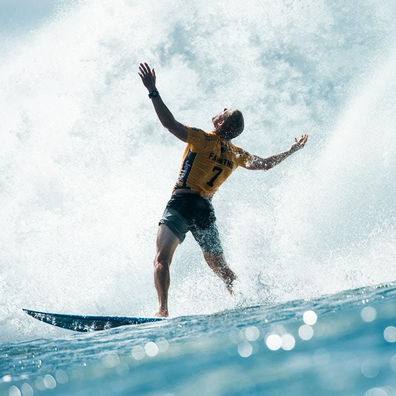 Mick Fanning standing on his surfboard celebrating a win.