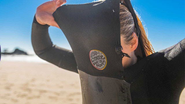 Surfer Conner Coffin changing into his E-Bomb Rip Curl wetsuit at a sunny Californian beach.