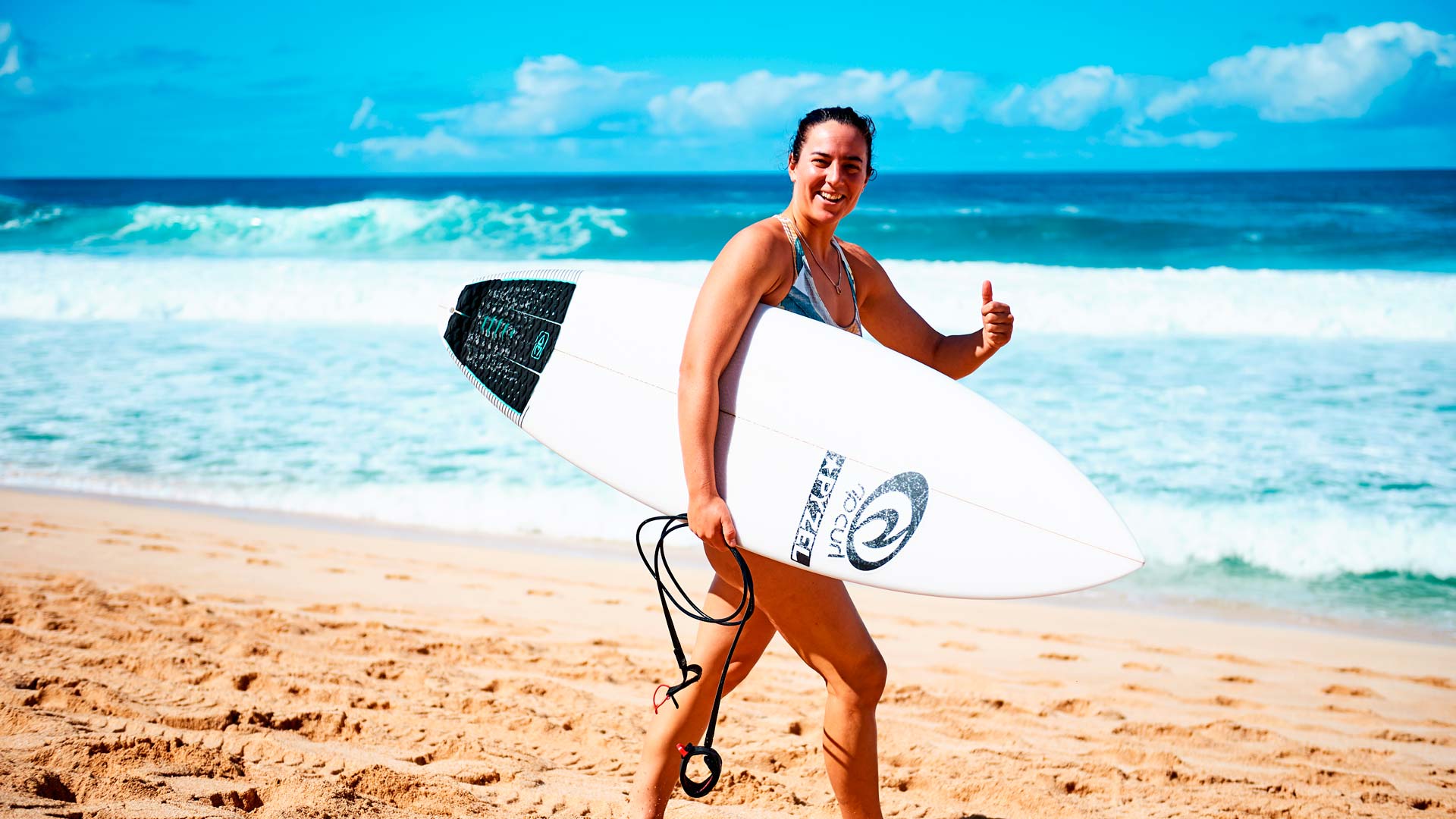 Tyler Wright giving the thumbs up carrying her board in Hawaii