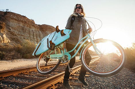 Rosy Hodge carrying a surfboard and a bike