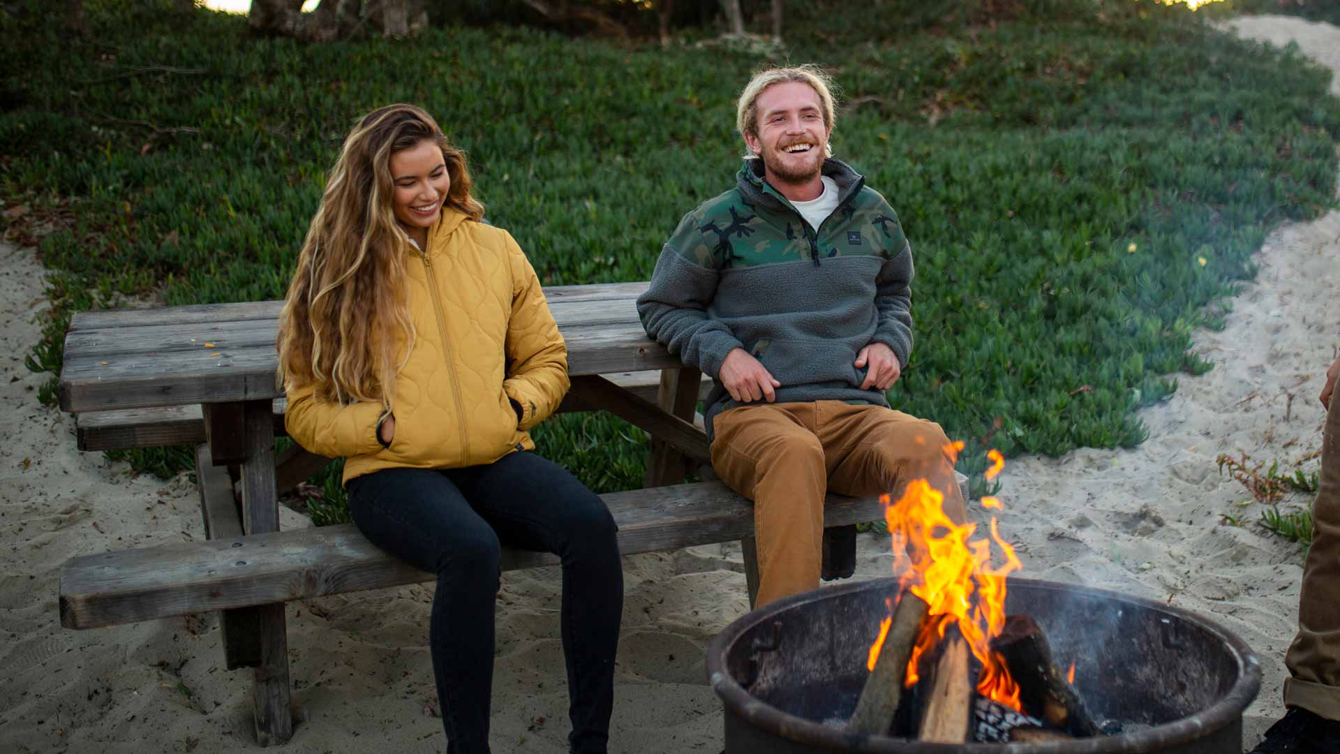 3 Rip Curl Surfers sitting around a fire wearing Anti-Series jackets